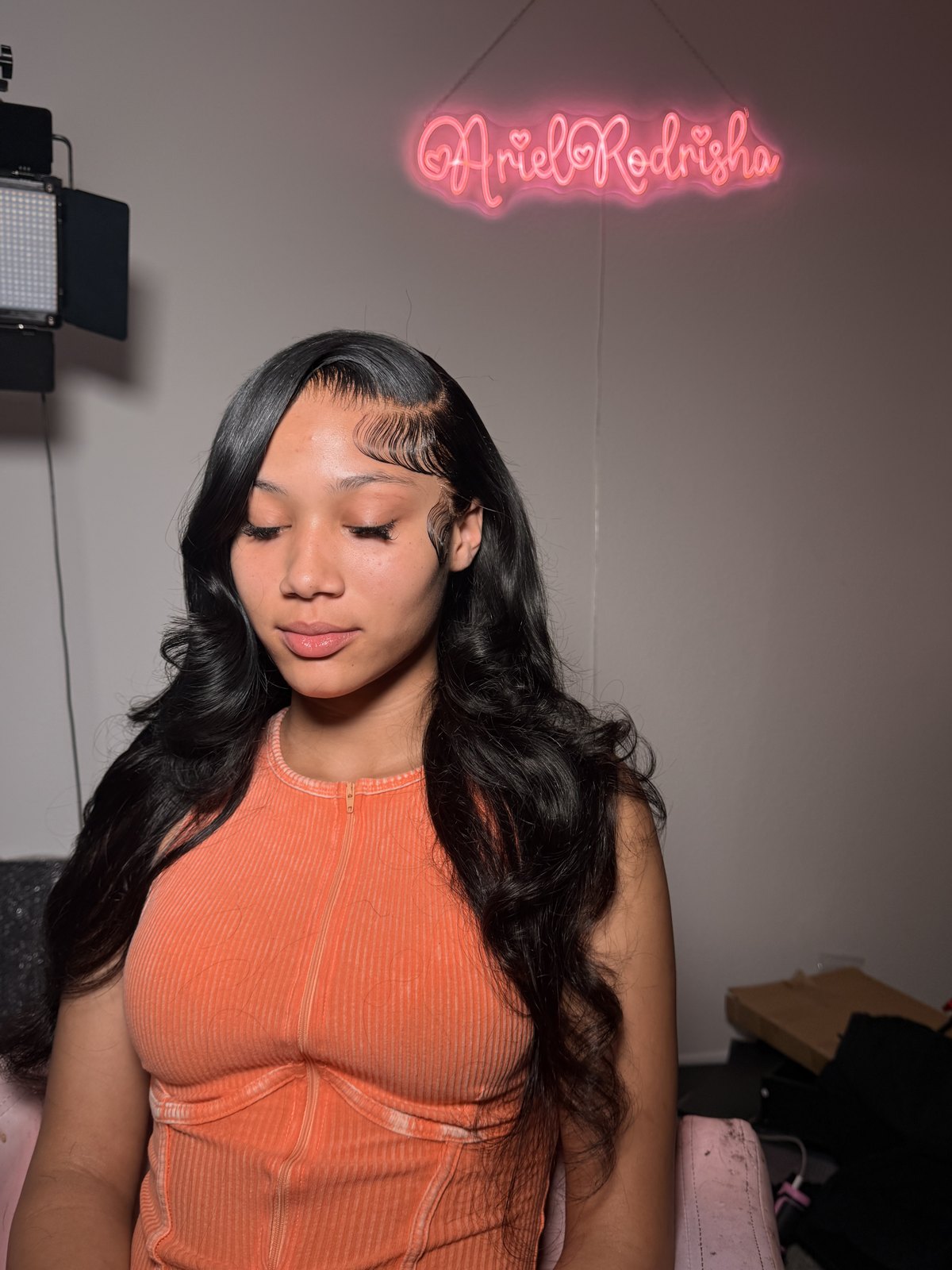 A long wavy lace-front install under the studio's neon name sign